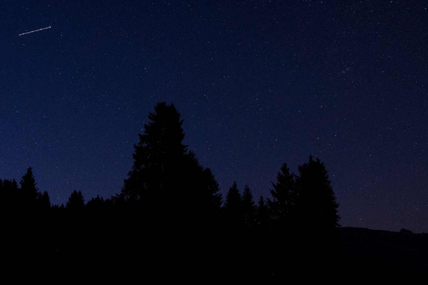 Fotografie des Nachthimmels in den Bergen. Aufnahmeort Falera in den Schweizer Alpen. Gut zu sehen sind Spuren der Positions- und Blitzlichter eines Flugzeugs.