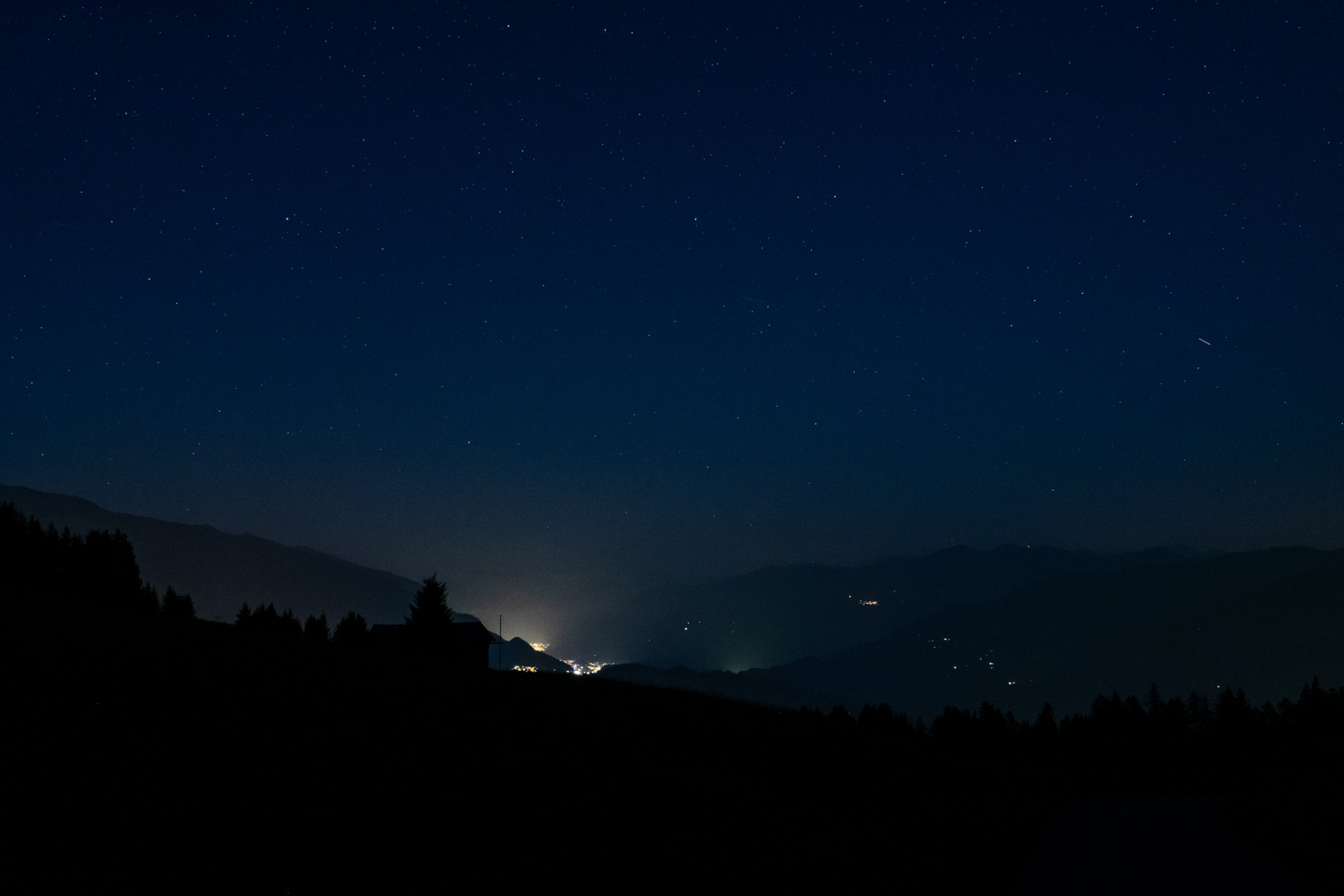 Fotografie des Nachthimmels in den Bergen. Aufnahmeort Falera in den Schweizer Alpen. Gut sichtbar ist die Lichtverschmutzung im Nachbardorf.