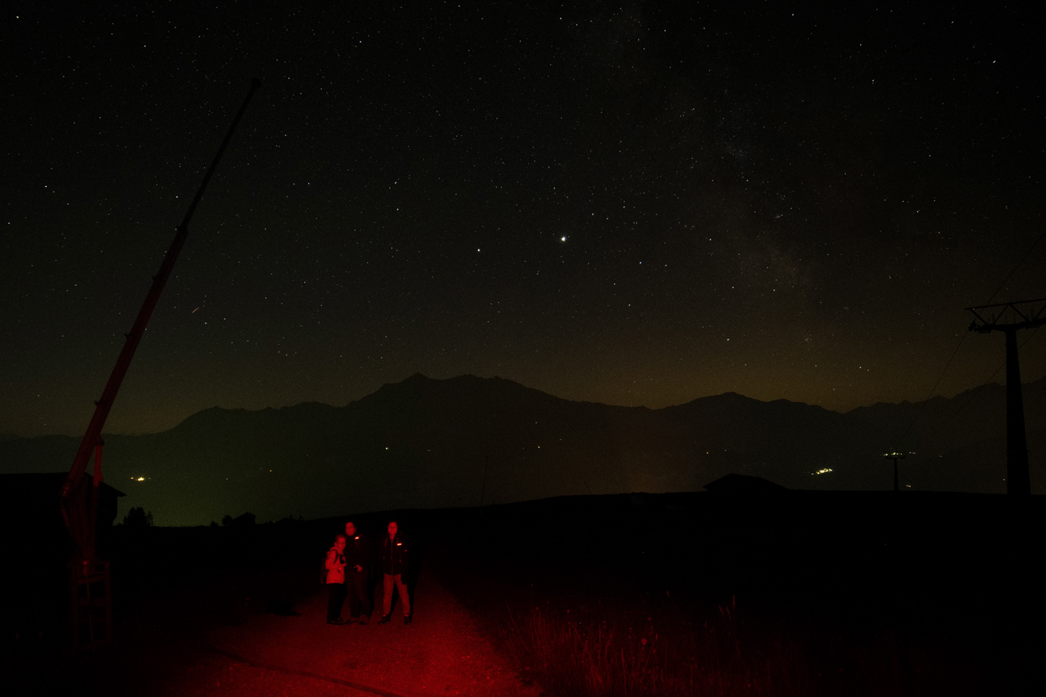 Fotografie des Nachthimmels bei Falera in den Schweizer Alpen. Bilder der Wanderer im roten Licht der Taschenlampe. 
