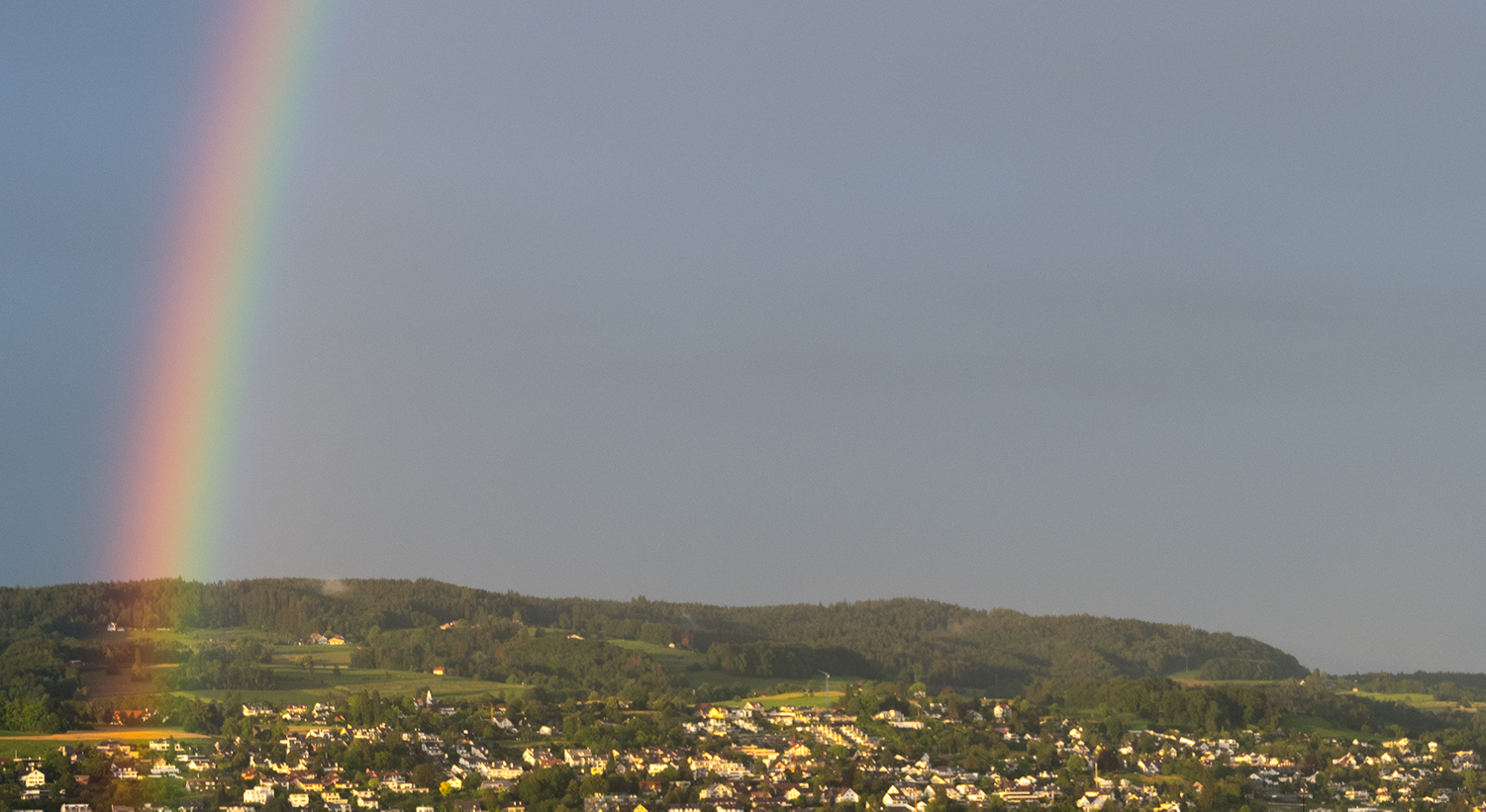 Fotografie eines Regenbogens bei Regenwetter. Gut zu sehen ist der Farbverlauf im Spektrum des Regenbogens. Aufnahmeort: Region Zürichsee.