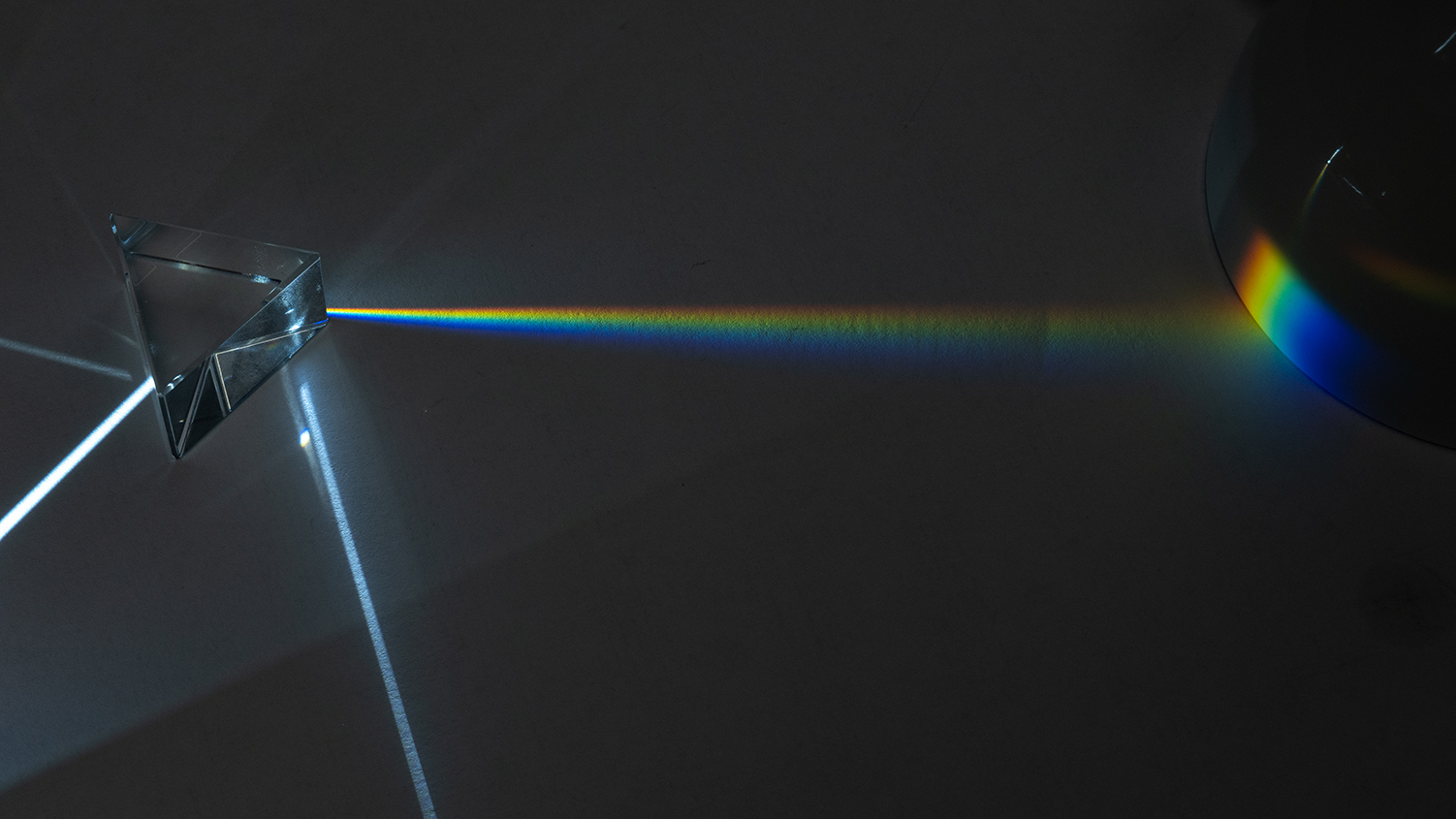 Fotografie eines Versuchsaufbaus mit weissem Licht, Spaltblende und Prisma. Projektion des Spektrums auf eine Oberfläche. Zerlegung von weissem Licht in seine sichtbaren Spektralkomponenten. 